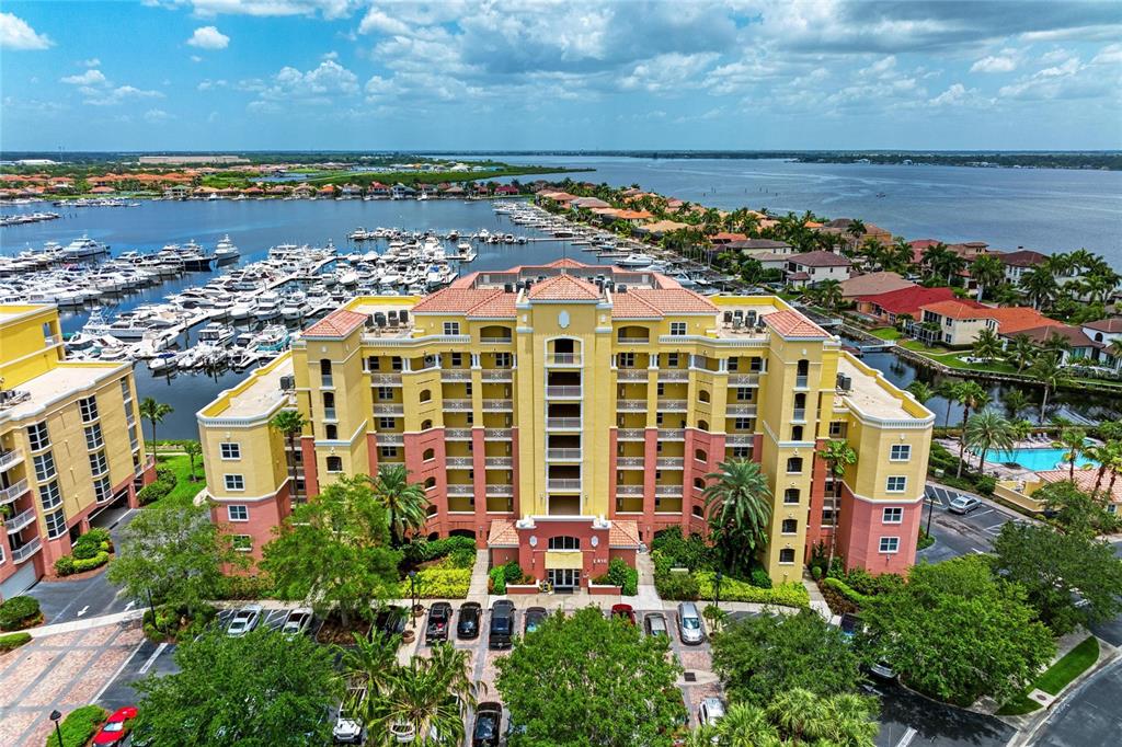 An aerial view shows a multi-story yellow and peach apartment building near a boat marina — 610 RIVIERA DUNES WAY UNIT 406, PALMETTO, FL