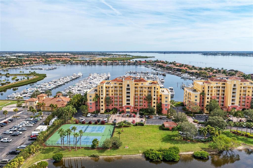 An aerial view shows a multi-story apartment complex with a tennis court and boat marina — 610 RIVIERA DUNES WAY UNIT 406, PALMETTO, FL