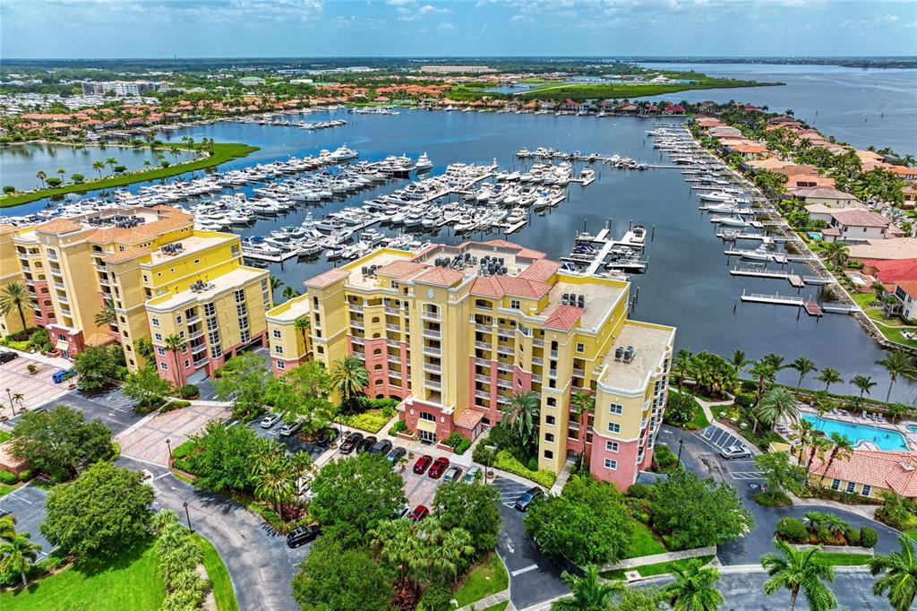 An aerial view shows a multi-story apartment complex situated beside a large boat marina — 610 RIVIERA DUNES WAY UNIT 406, PALMETTO, FL