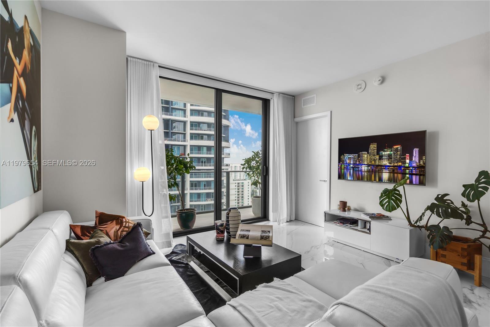 A modern living room features white marble floors, a white sectional sofa, and a balcony view — 1300 S Miami Ave # 2508, Miami FL 33130, MIAMI, FL
