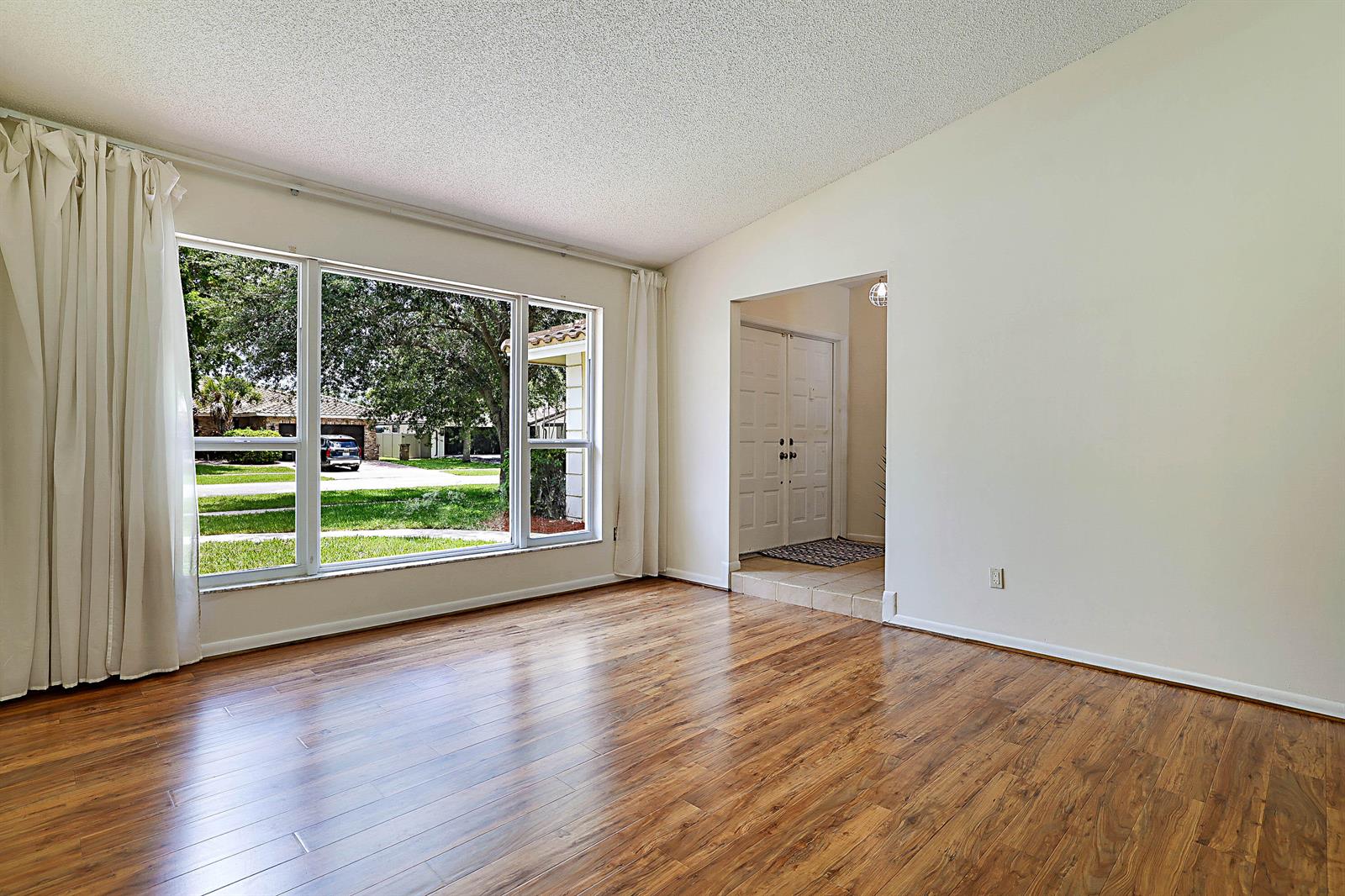 An empty room with wood-look flooring, a large window, and an entryway with double doors — 20869 Sonrisa Way, Boca Raton FL 33433, BOCA RATON, FL