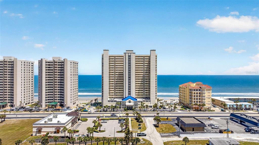 An aerial view shows high-rise oceanfront condominiums and commercial buildings near a sandy beach — 3333 S ATLANTIC AVENUE UNIT 2202, DAYTONA BEACH, FL