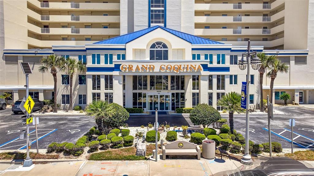 The exterior of the Grand Coquina building features a blue roof and a paved entrance — 3333 S ATLANTIC AVENUE UNIT 2202, DAYTONA BEACH, FL