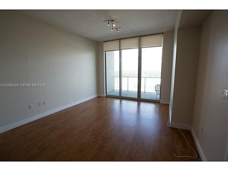 An empty room with wood-look flooring, beige walls, and a sliding glass door to a balcony — 3470 E Coast Ave # H1503, Miami FL 33137, MIAMI, FL