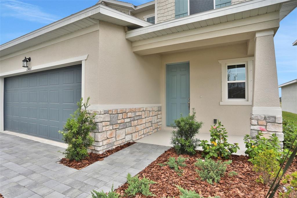 The exterior of a house features a gray garage door, stone veneer, and a blue door — 8112 SUNNY POINT TRAIL, PARRISH, FL