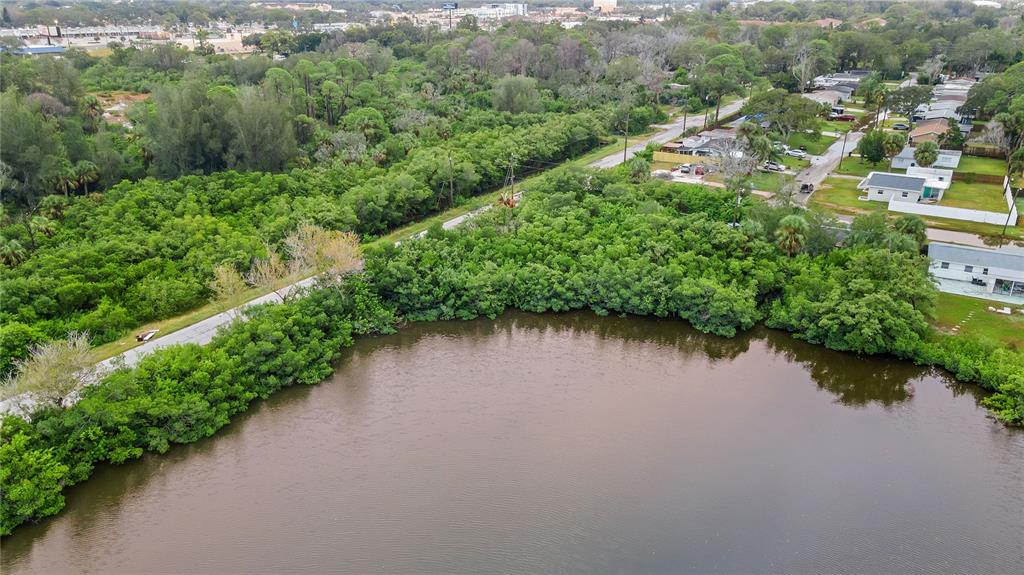 An aerial view shows a body of water bordered by dense trees and nearby houses — 4935 LARGO TERRACE, NEW PORT RICHEY, FL