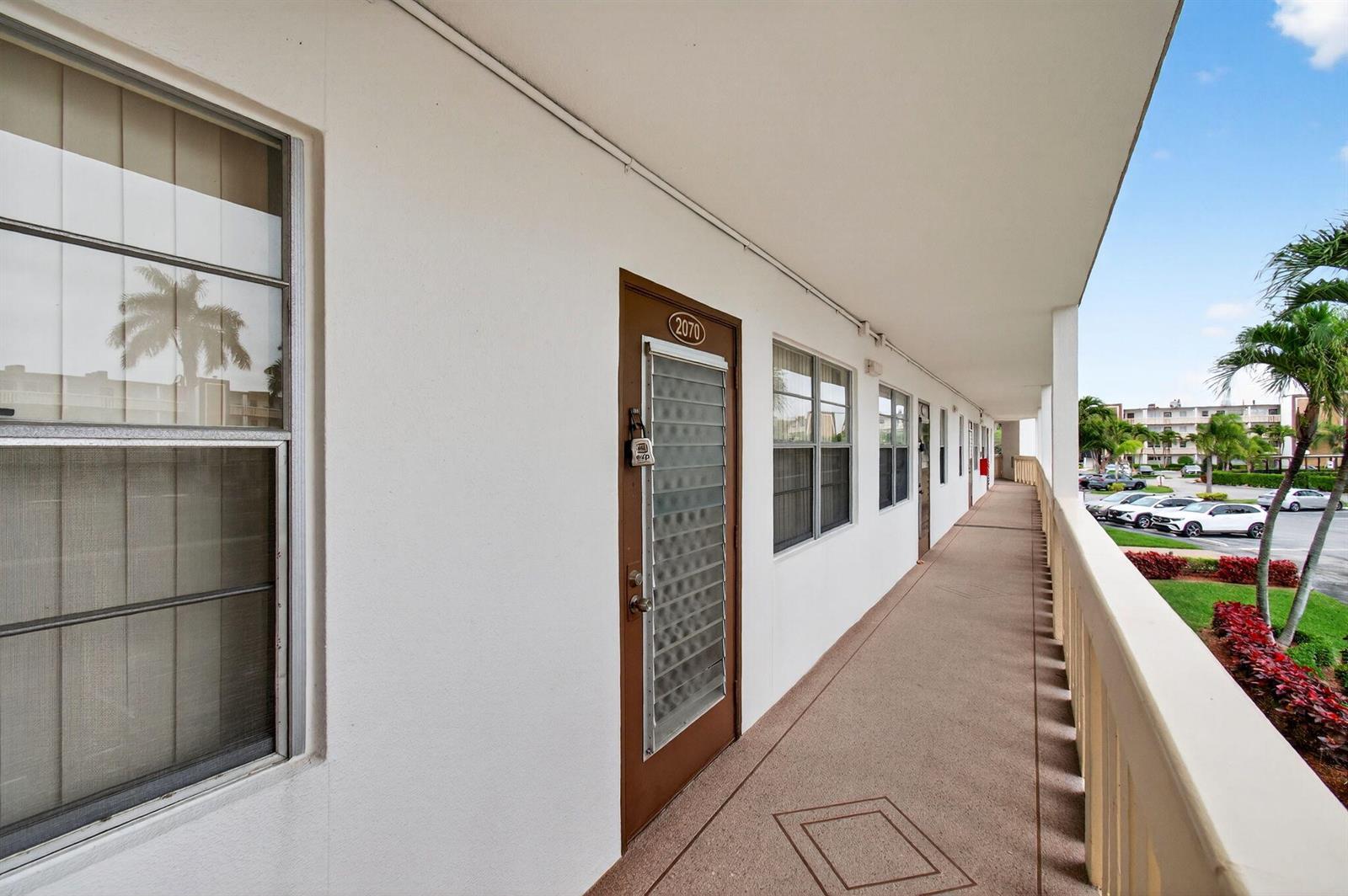 An exterior walkway of a multi-story building features a brown door numbered 2070 — 2070 Guildford D, Boca Raton FL 33434, BOCA RATON, FL