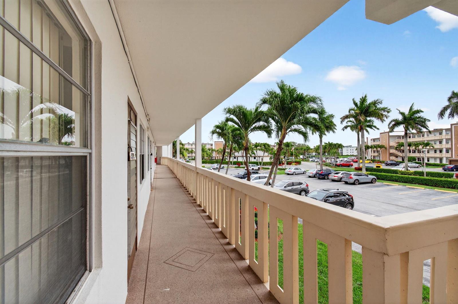An outdoor walkway with a beige railing overlooks a parking lot and palm trees — 2070 Guildford D, Boca Raton FL 33434, BOCA RATON, FL
