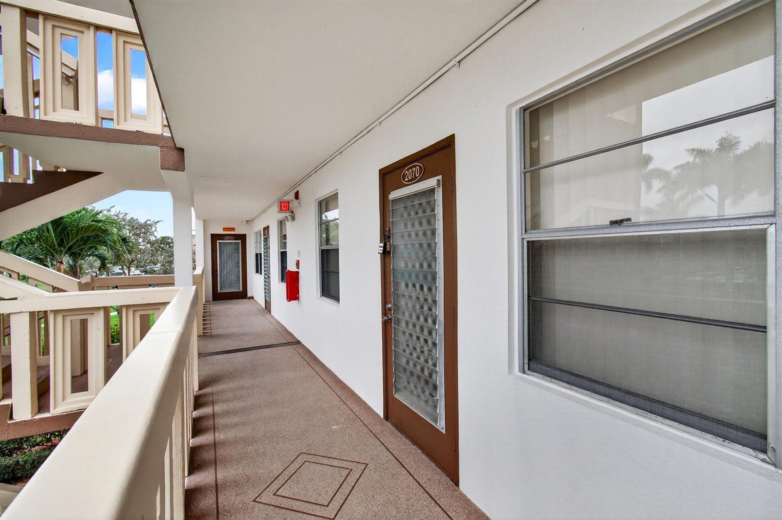 An exterior walkway with brown doors, windows, and a staircase in a multi-story apartment building — 2070 Guildford D, Boca Raton FL 33434, BOCA RATON, FL