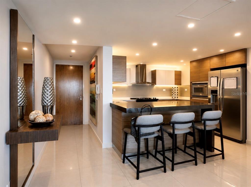 A modern kitchen features a breakfast bar with three stools, stainless steel appliances, and wood cabinetry — 48 LUIS MUÑOZ RIVERA UNIT 2202, SAN JUAN, PR