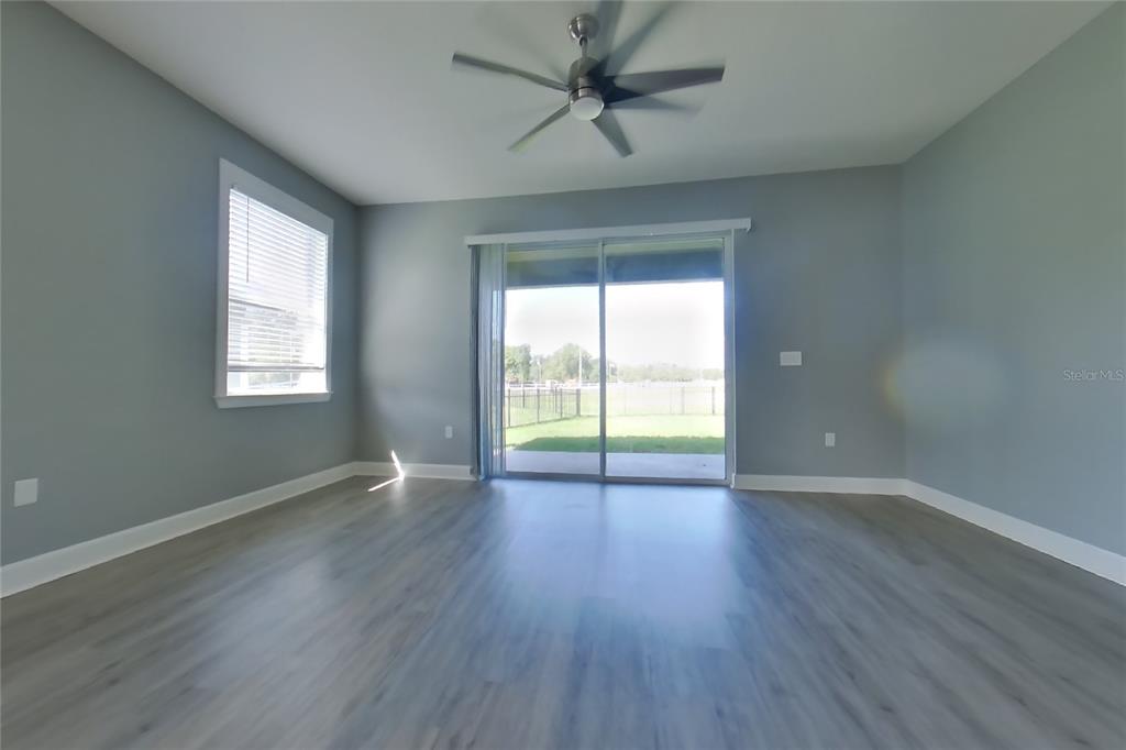 An empty room features gray walls, light wood-look flooring, a ceiling fan, and sliding glass doors — 2416 SABASTIAN STREET, MOUNT DORA, FL