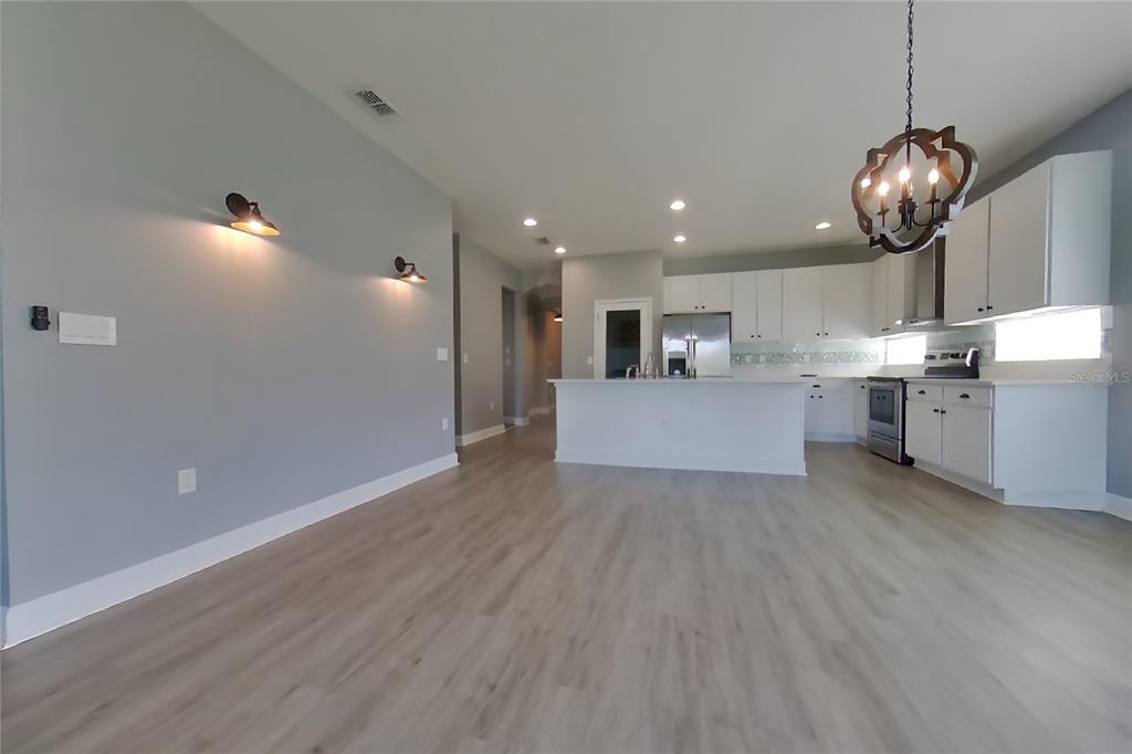 A kitchen with white cabinets and a center island opens into a light-gray living area — 2416 SABASTIAN STREET, MOUNT DORA, FL