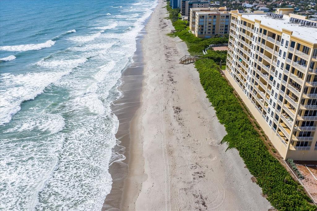 An aerial view of a sandy beach next to a large multi-story apartment building — 1025 HIGHWAY A1A UNIT 406, SATELLITE BEACH, FL