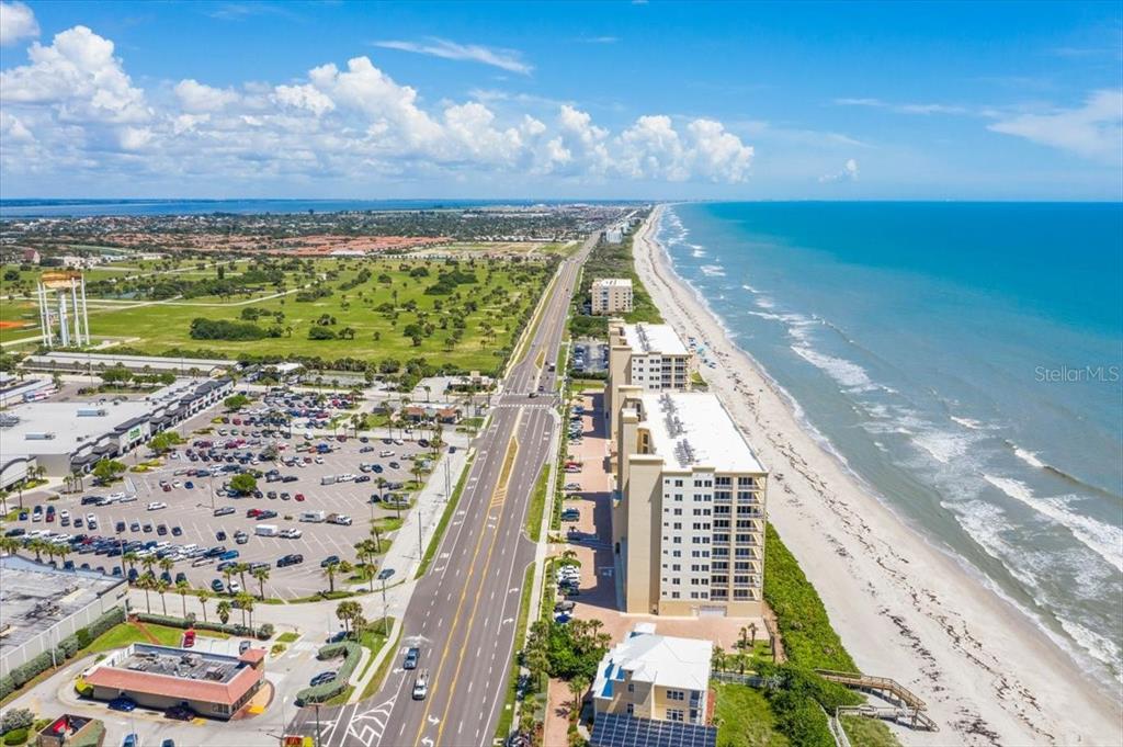 An aerial view shows a coastal highway running between a beach and a large parking lot — 1025 HIGHWAY A1A UNIT 406, SATELLITE BEACH, FL
