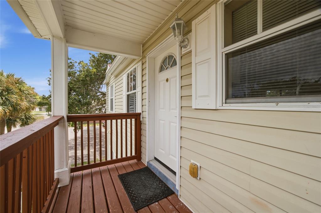 A wooden porch with a railing leads to a white front door and a window — 9019 COCHISE LANE UNIT 201, PORT RICHEY, FL