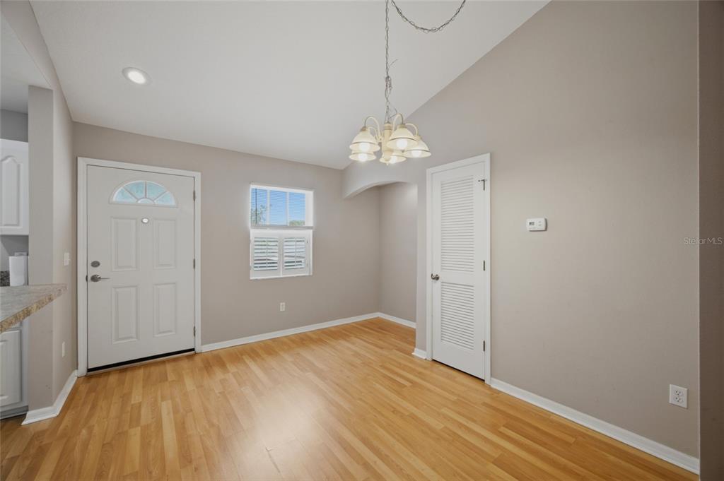 A dining area features light wood flooring, a white door, a window, and a chandelier — 9019 COCHISE LANE UNIT 201, PORT RICHEY, FL