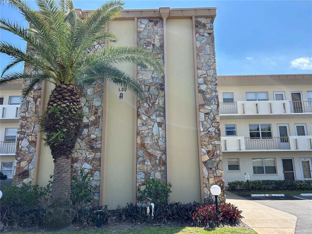 A three-story apartment building exterior features stone accents, a palm tree, and metal balconies — 4480 IRONWOOD CIRCLE UNIT 213A, BRADENTON, FL