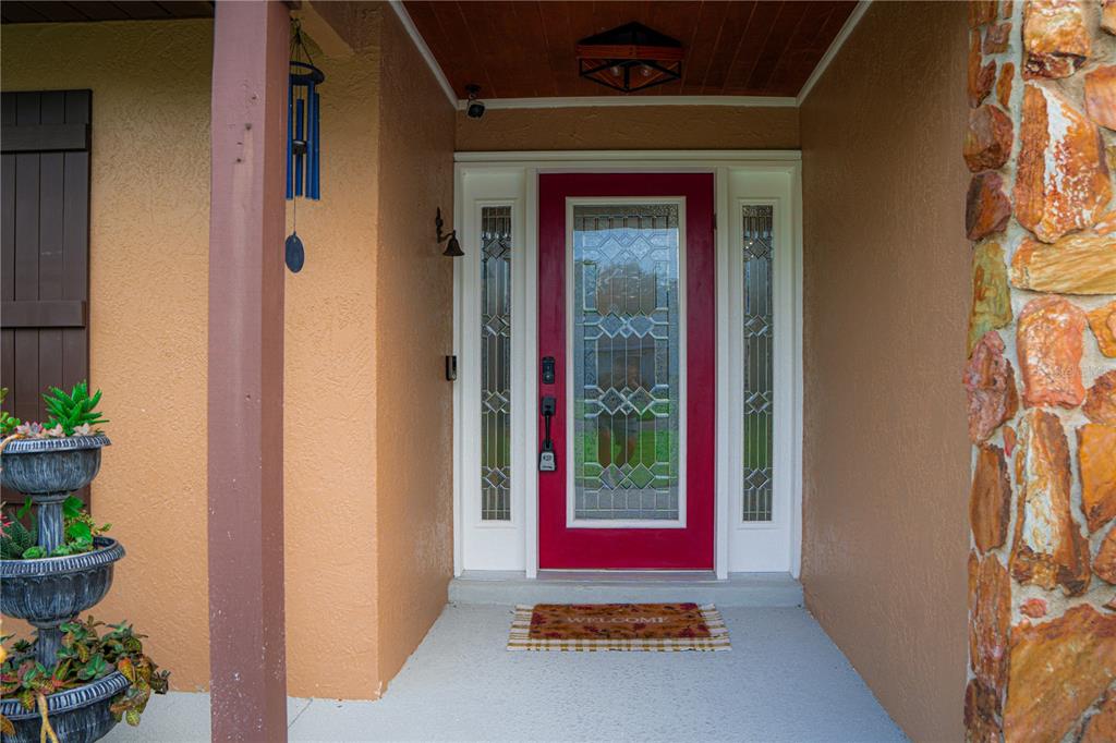 A red front door with glass panels is centered under a covered entryway with stone — 5834 98TH AVENUE N, PINELLAS PARK, FL
