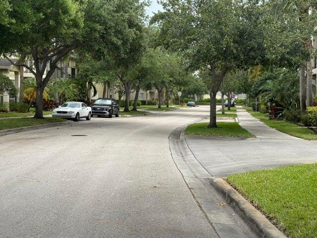 A residential street lined with mature trees, sidewalks, and parked cars on a sunny day — 2131 SE Destin Drive, FL 34952, FL