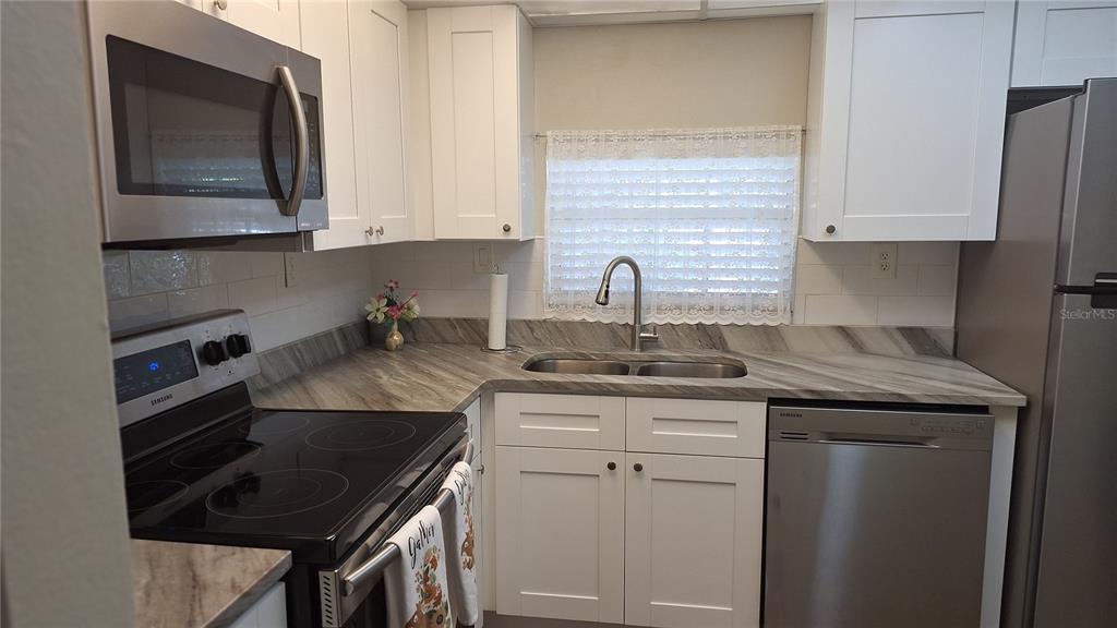 A kitchen features white cabinets, stainless steel appliances, and a gray patterned countertop — 809 RUSSELL LANE UNIT 323, BRANDON, FL