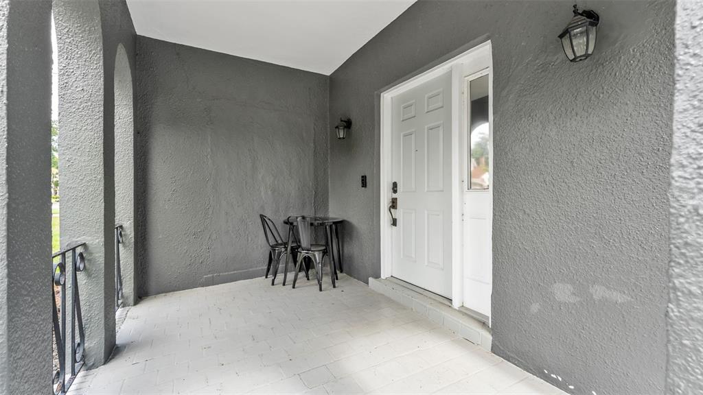 A covered porch with gray stucco walls, a light-colored tiled floor, and a white door — 630 E STANFORD STREET, BARTOW, FL