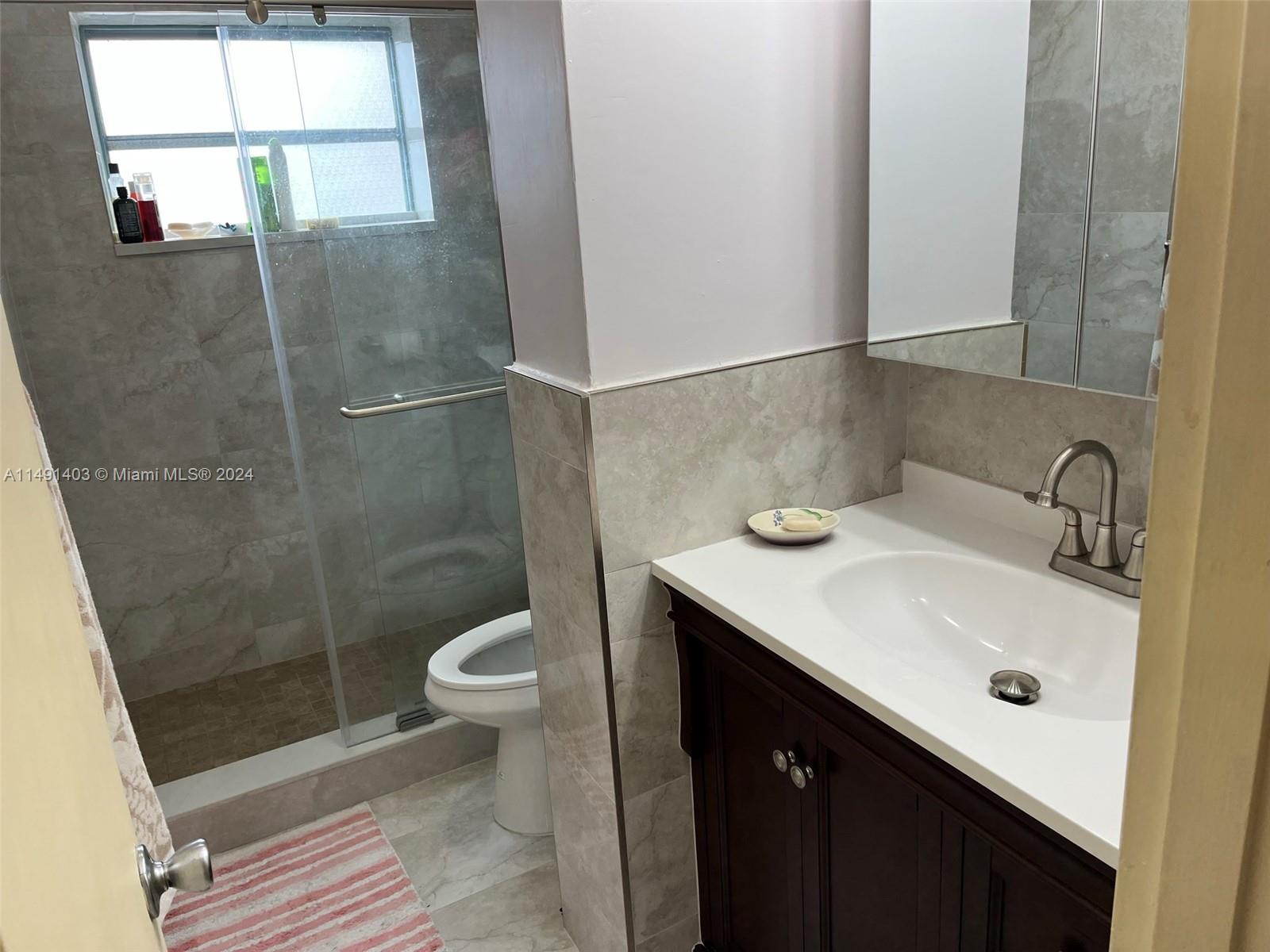 A bathroom features a dark wood vanity, a glass-enclosed shower, and light-colored tile walls — 181 NE 14th Ave # 22B, Hallandale Beach FL 33009, HALLANDALE BEACH, FL