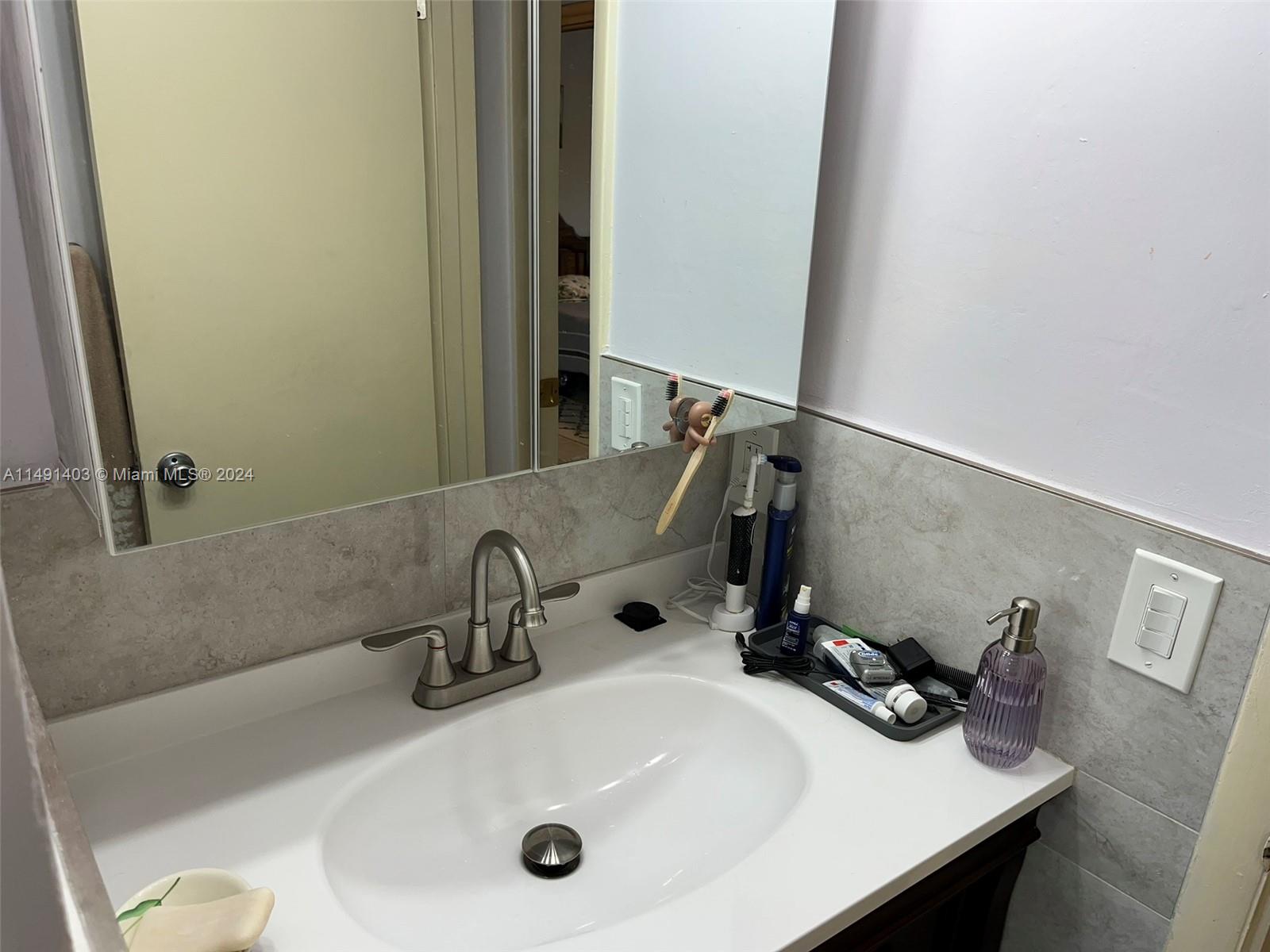 A bathroom vanity features a white sink, brushed nickel faucet, and a wall-mounted mirror — 181 NE 14th Ave # 22B, Hallandale Beach FL 33009, HALLANDALE BEACH, FL