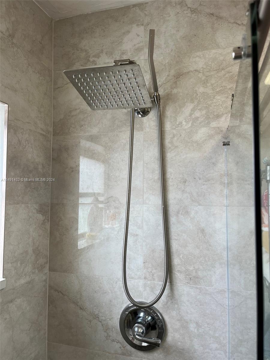 A shower features a square rainfall showerhead, a handheld sprayer, and light-colored stone tile walls — 181 NE 14th Ave # 22B, Hallandale Beach FL 33009, HALLANDALE BEACH, FL