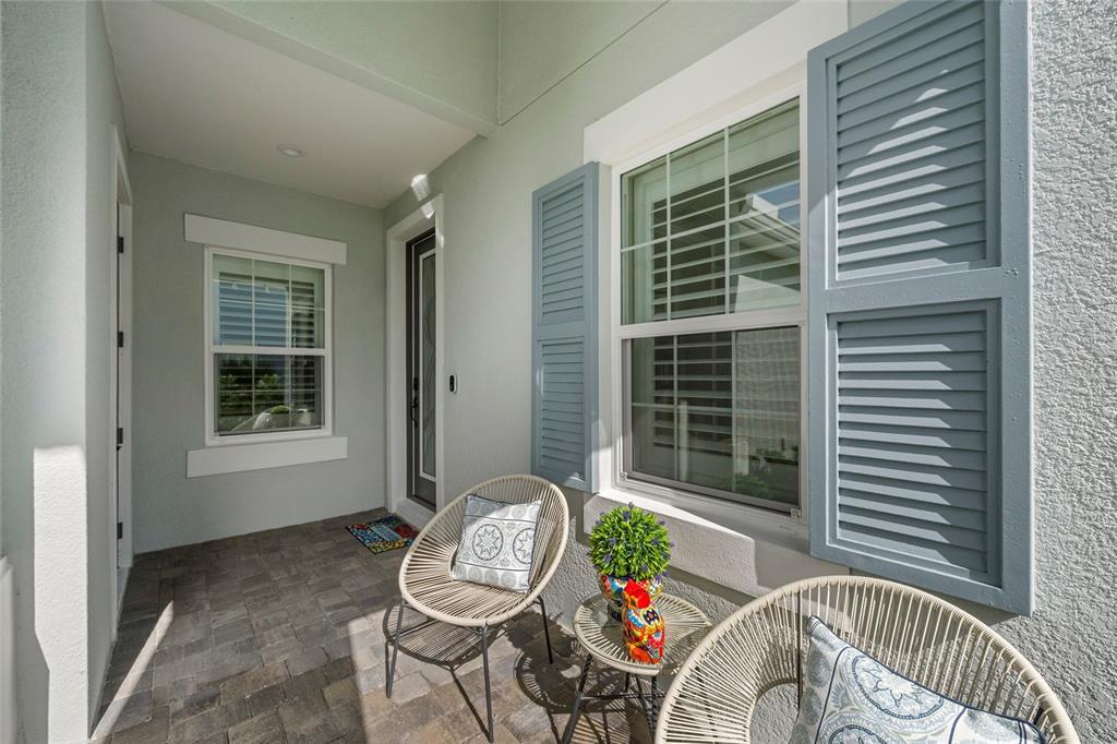 A covered front porch features two woven chairs, a small table, and blue window shutters — 10169 LAKE WALES CIRCLE, SARASOTA, FL