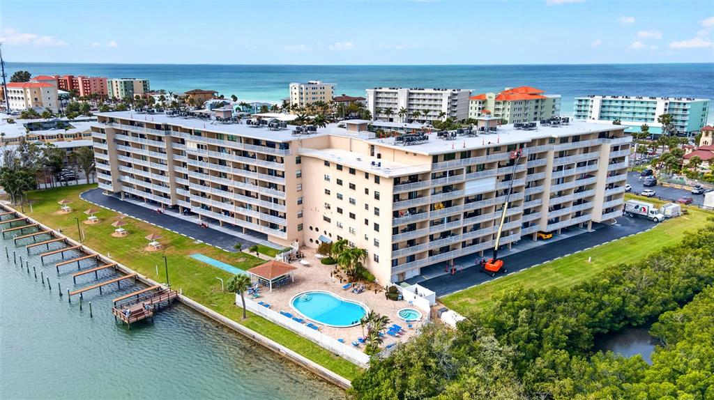 An aerial view shows a large multi-story apartment building with a pool and boat docks — 19451 GULF BOULEVARD UNIT 204, INDIAN SHORES, FL