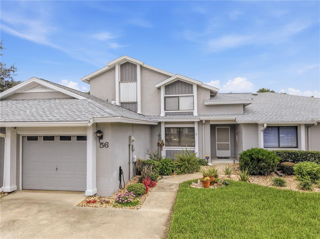 A gray, two-story house features a single-car garage, a front walkway, and a landscaped yard — 56 LAKE FOREST PLACE, PALM COAST, FL