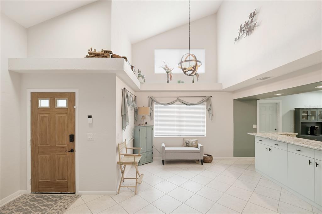 A bright entryway features a vaulted ceiling, tiled floors, a wooden door, and kitchen cabinetry — 56 LAKE FOREST PLACE, PALM COAST, FL