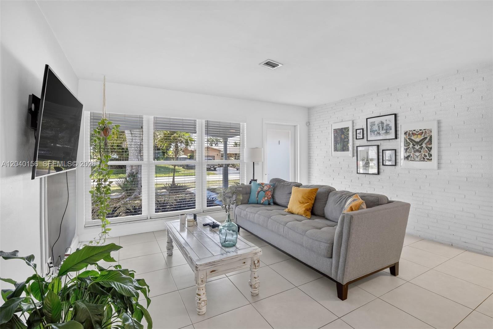 A living room features a grey sofa, white brick wall, and a rustic coffee table — 2220 N 40th Ave, Hollywood FL 33021, HOLLYWOOD, FL