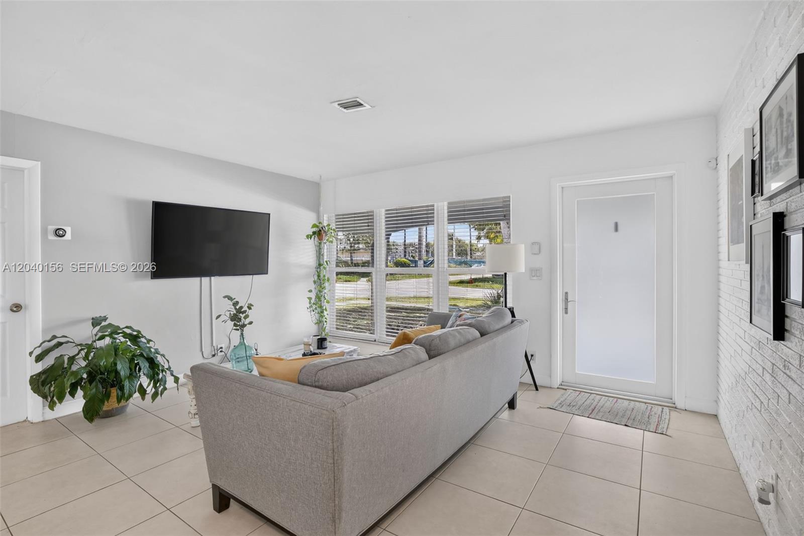 A living room features a gray sofa, a wall-mounted television, and tile flooring — 2220 N 40th Ave, Hollywood FL 33021, HOLLYWOOD, FL