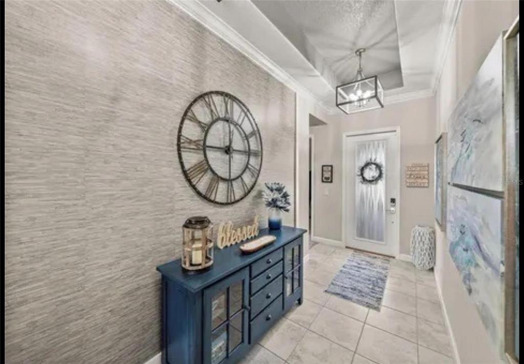 A foyer features a blue console table, a large wall clock, and a textured accent wall — 31475 CABANA RYE AVENUE, SAN ANTONIO, FL
