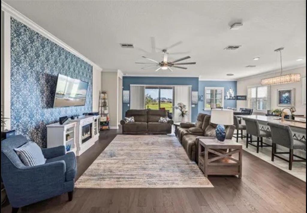 An open-concept living room and kitchen featuring blue accent walls, a fireplace, and tile flooring — 31475 CABANA RYE AVENUE, SAN ANTONIO, FL