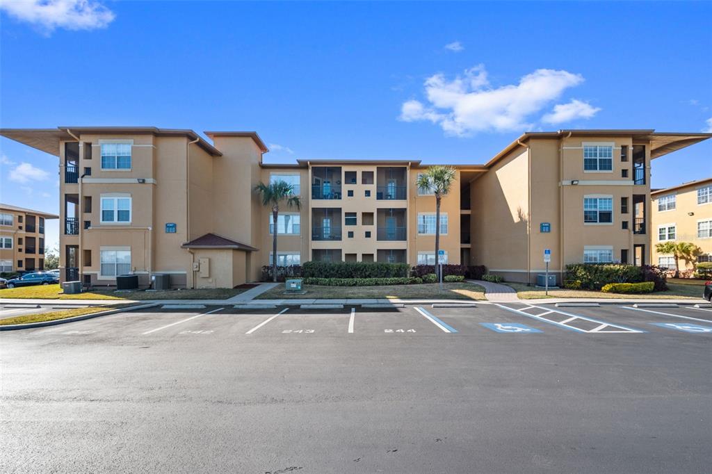 A three-story apartment building with tan stucco walls stands behind a paved parking lot — 4305 BAYSIDE VILLAGE DRIVE UNIT 202, TAMPA, FL