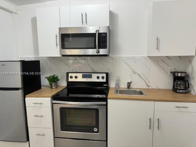 A compact kitchen features white cabinets, stainless steel appliances, and a marble-patterned backsplash — 1270 NE 210th Ter # B, Miami FL 33179, MIAMI, FL