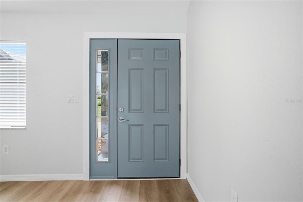 A blue front door with a side window light stands in a room with light-colored walls — 6426 JULY AVENUE, SPRING HILL, FL