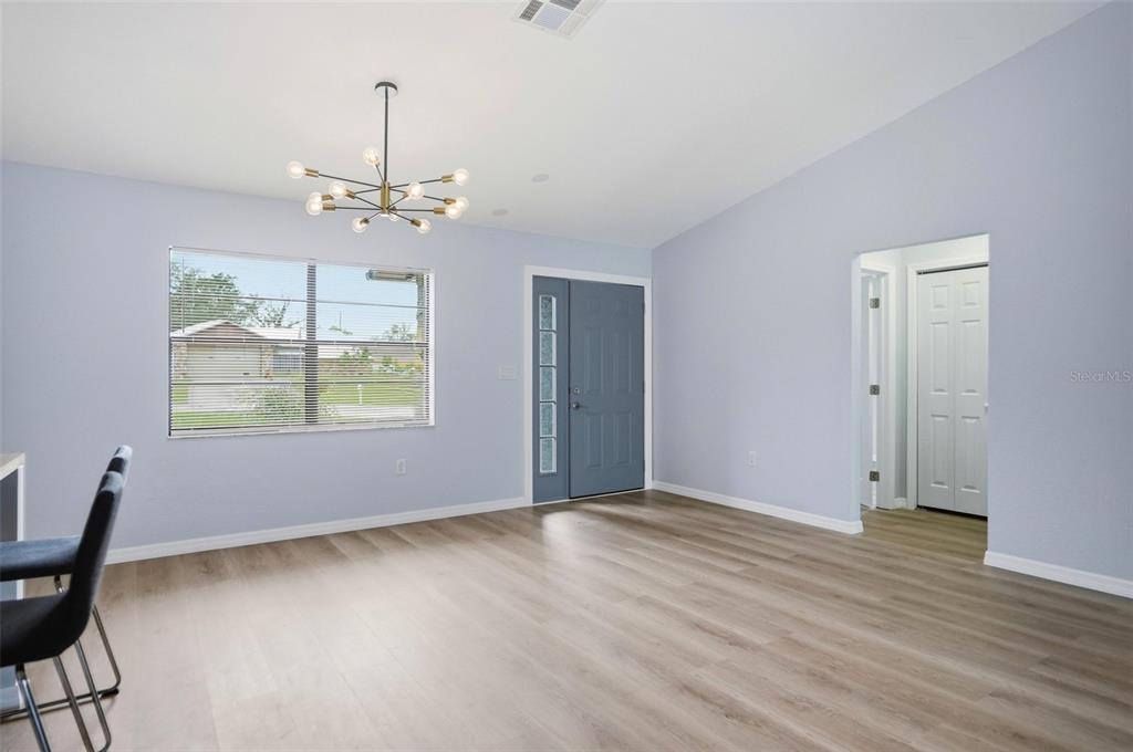 A living room with light blue walls, wood-look flooring, a modern chandelier, and a front door — 6426 JULY AVENUE, SPRING HILL, FL