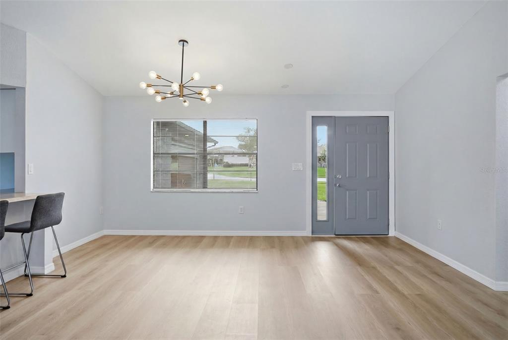 A dining area with light wood flooring, a modern chandelier, and a gray front door — 6426 JULY AVENUE, SPRING HILL, FL