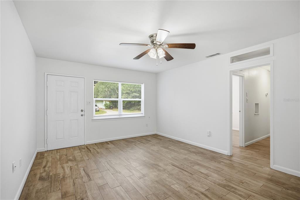 A bright room with white walls, wood-look tile flooring, a ceiling fan, and a door — 1318 NE 14TH STREET, GAINESVILLE, FL