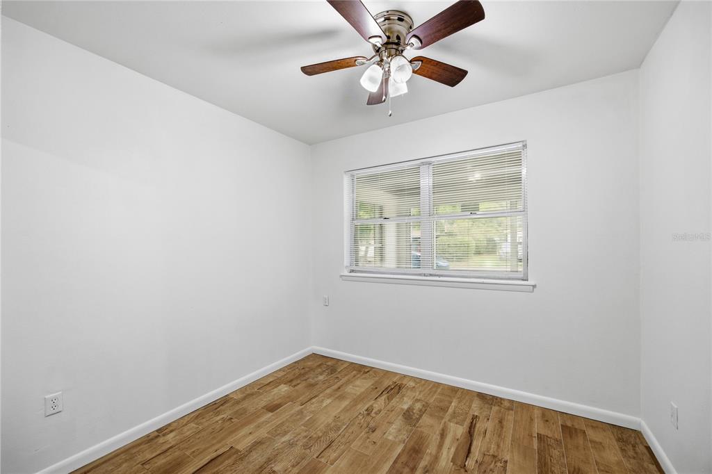 An empty bedroom features white walls, wood-look tile flooring, a ceiling fan, and a window — 1318 NE 14TH STREET, GAINESVILLE, FL