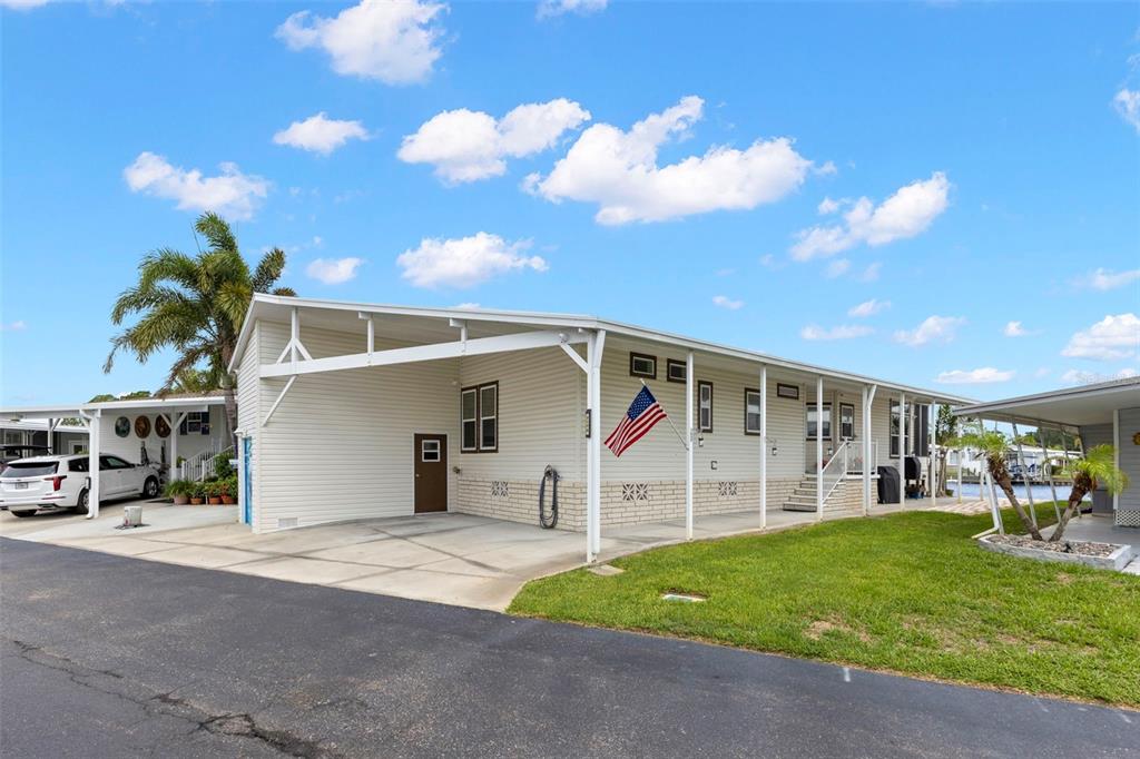 A single-story manufactured home with a carport, white siding, and an American flag — 7174 MOUNT ARLINGTON DRIVE NE UNIT 419, ST PETERSBURG, FL