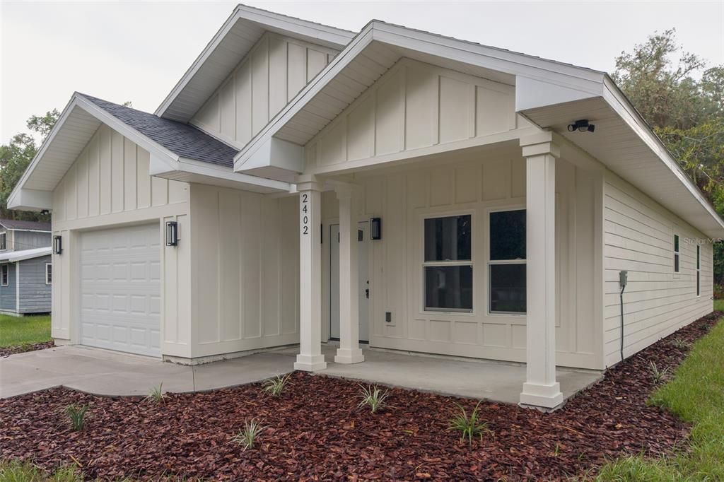 A single-story house with white board-and-batten siding, a front porch, and a one-car garage — 2402 NE 70TH STREET, GAINESVILLE, FL