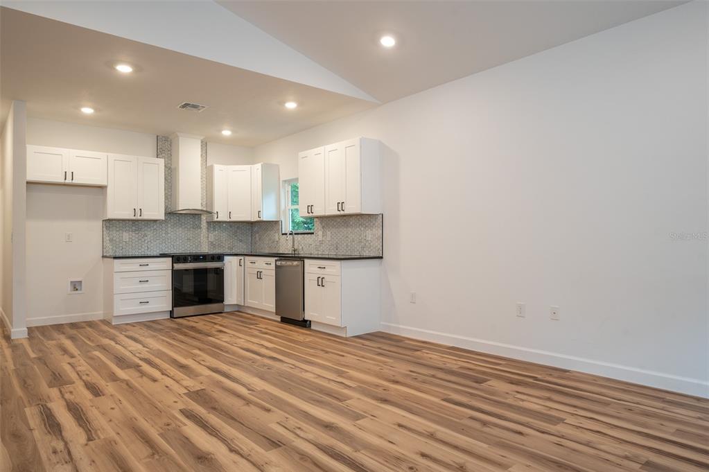 A kitchen features white cabinets, stainless steel appliances, a tiled backsplash, and wood-look flooring — 2402 NE 70TH STREET, GAINESVILLE, FL