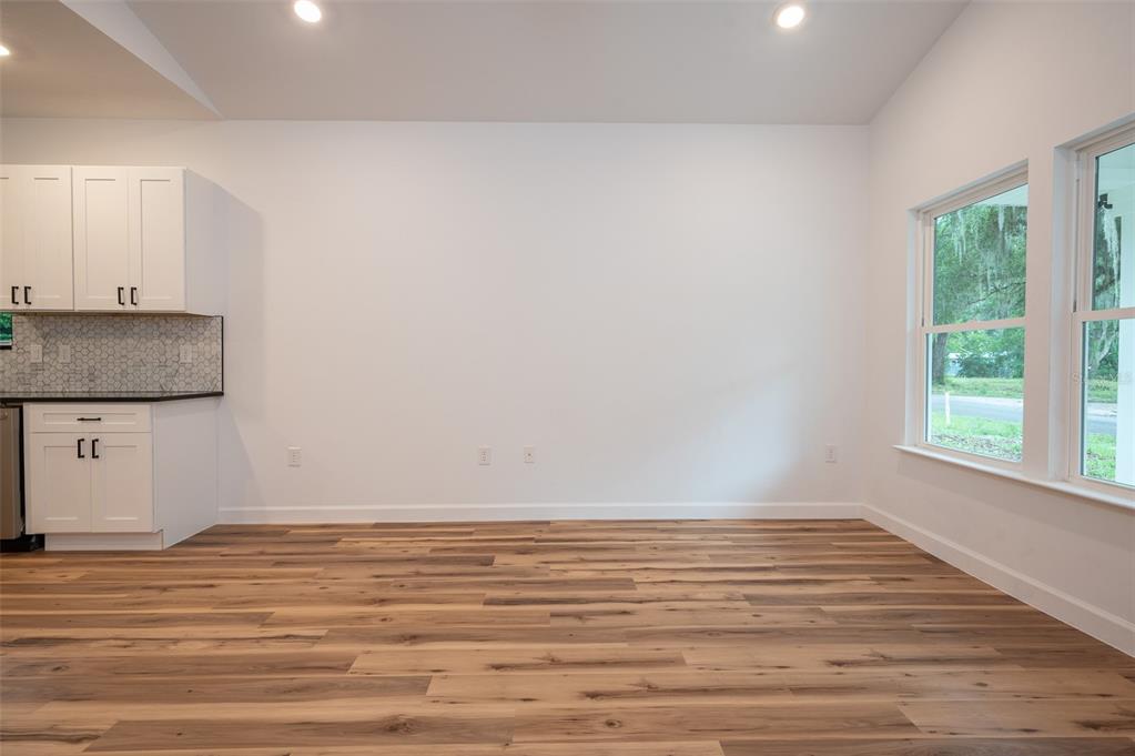 A bright, empty room features white walls, wood-look flooring, white cabinets, and two large windows — 2402 NE 70TH STREET, GAINESVILLE, FL