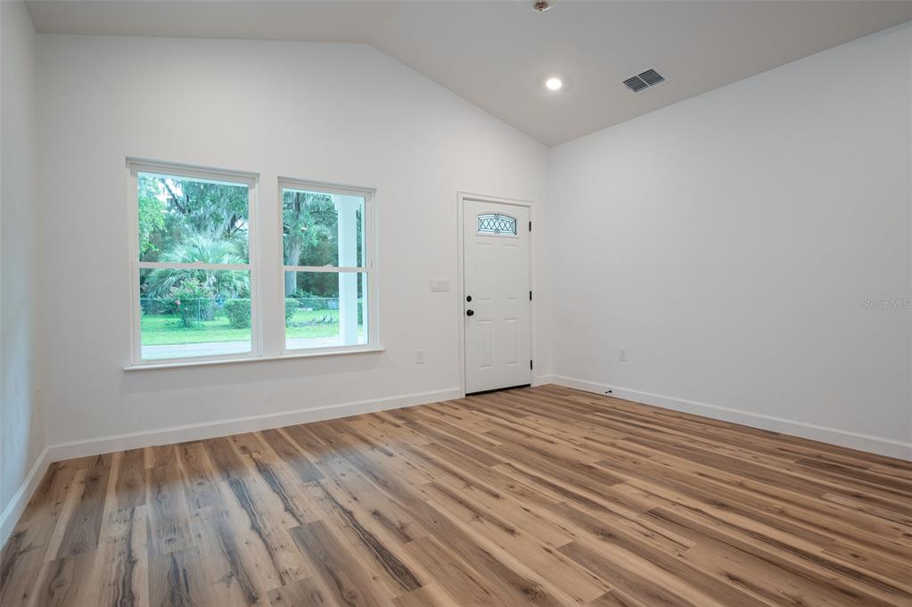 An empty room features white walls, a vaulted ceiling, wood-look flooring, and a front door — 2402 NE 70TH STREET, GAINESVILLE, FL