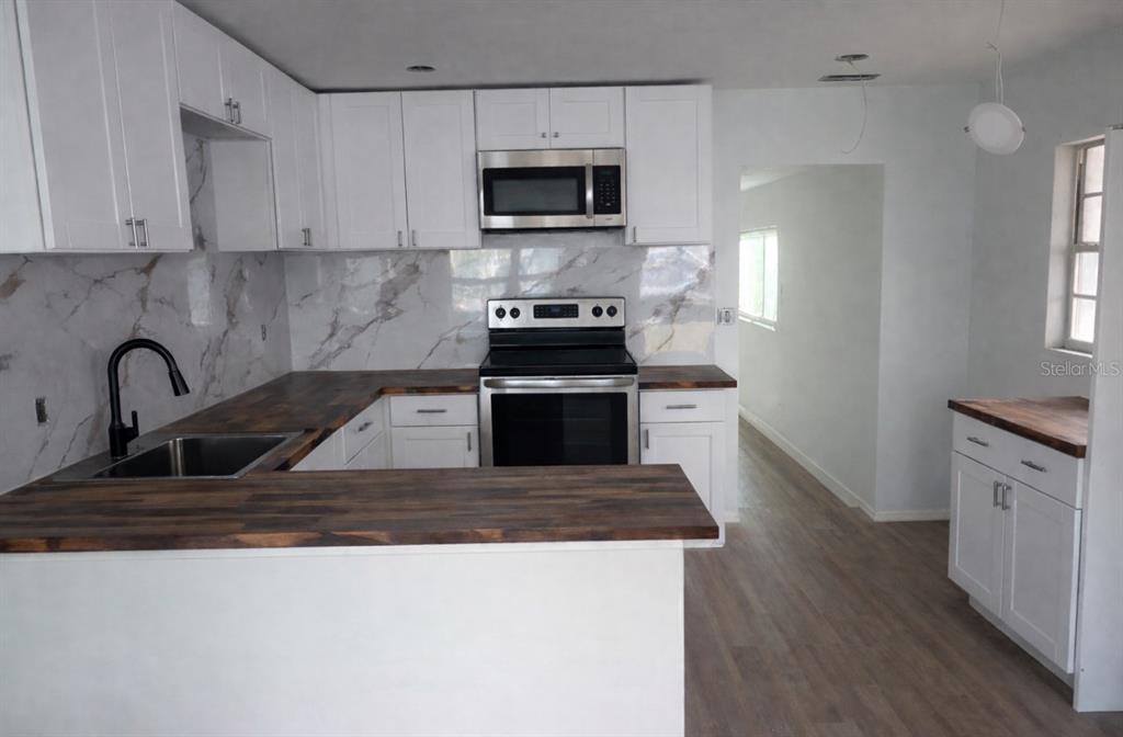 A kitchen features white cabinets, dark wood countertops, a marble backsplash, and stainless steel appliances — 2442 40TH AVENUE N, ST PETERSBURG, FL