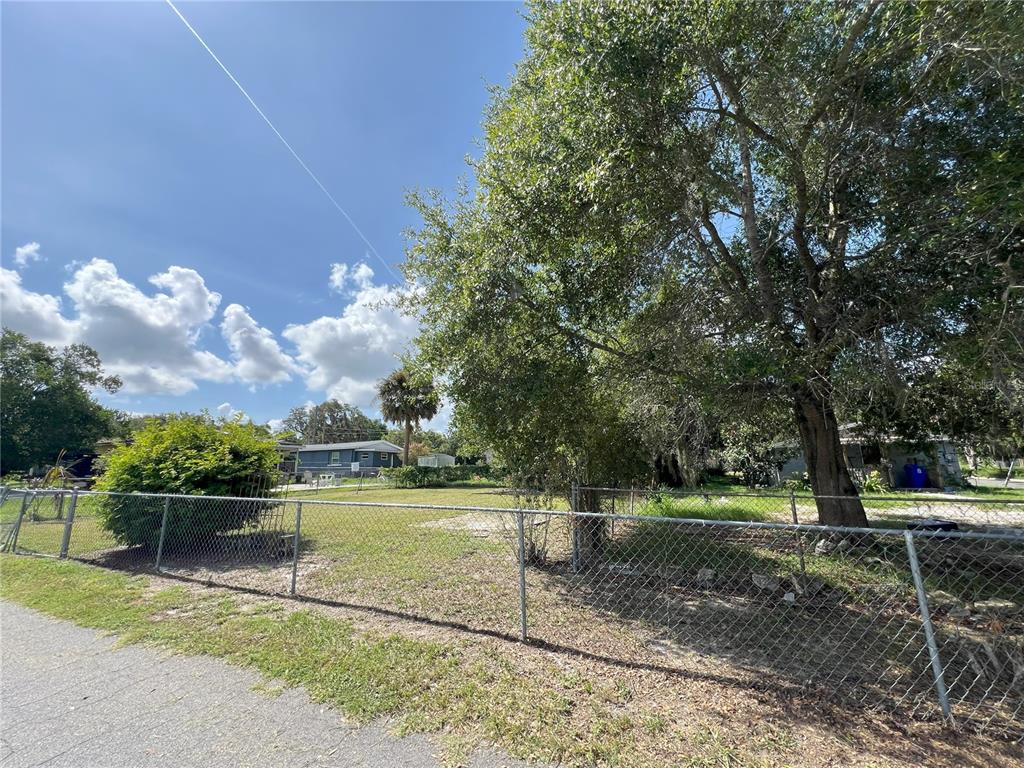 A chain-link fence encloses a grassy lot with several trees under a blue sky — 510 PICKENS STREET, LAKELAND, FL